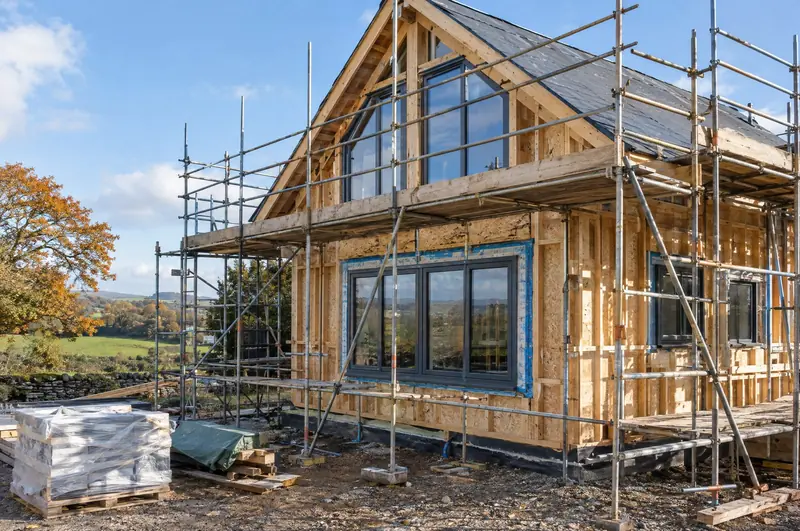 Timber-frame self-build under scaffolding with new grey windows fitted